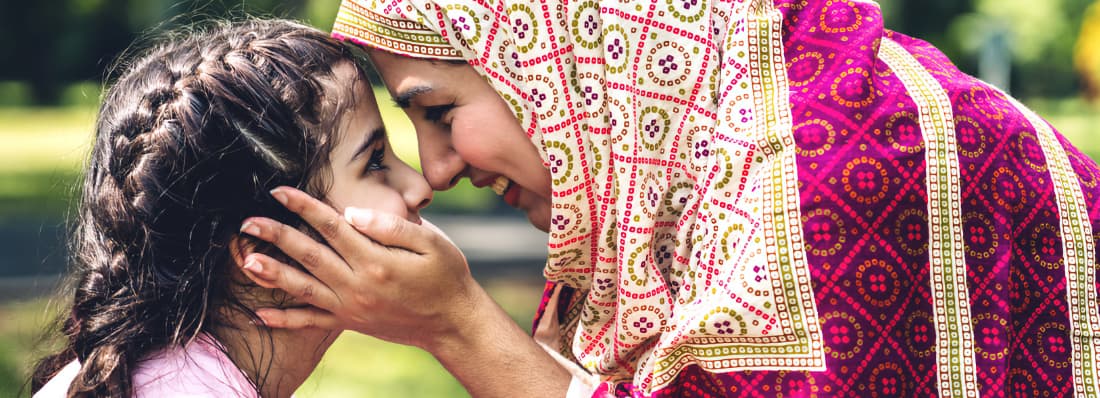 A smiling Muslim mother holds her daughter's face
